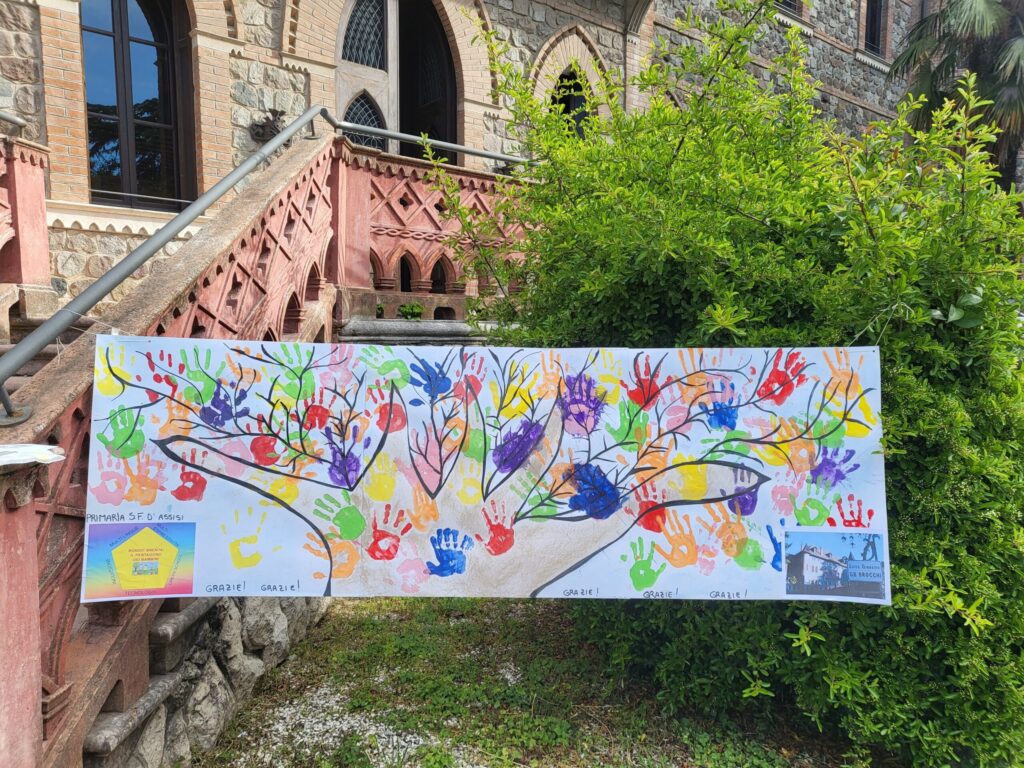Manifesto donato dalla Primaria al Liceo: stampo di tutte le mani dei bambini in un albero con ringraziamenti. Appeso davanti al castello